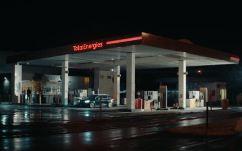 Image tirée de la campagne des 30 ans du Club TotalEnergies, où l'on voit la station service de nuit avec une voiture prêt de la pompe et un homme qui sort de la boutique